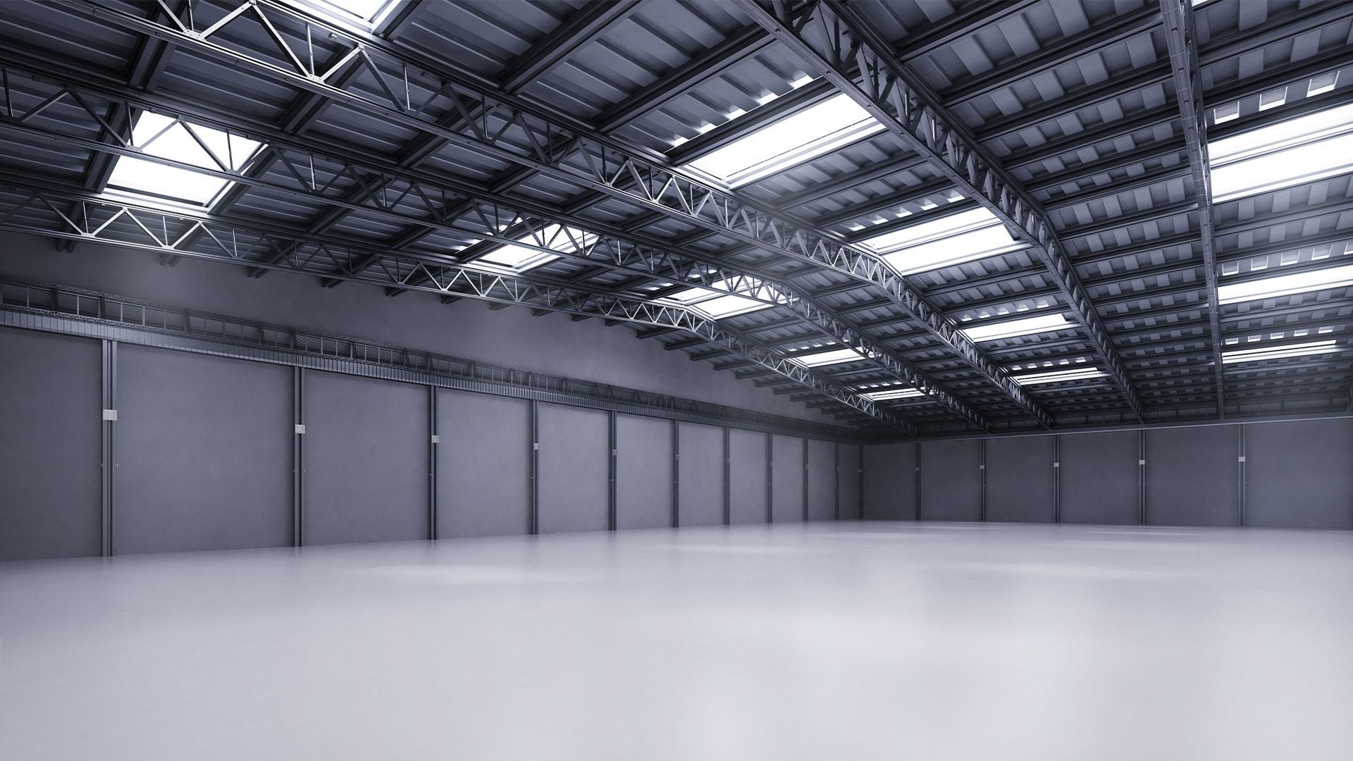 A wide-angle interior view of a modern logistics warehouse in Europe, showcasing prime industrial real estate with high ceilings, polished concrete floors, and a steel truss roof with skylights.