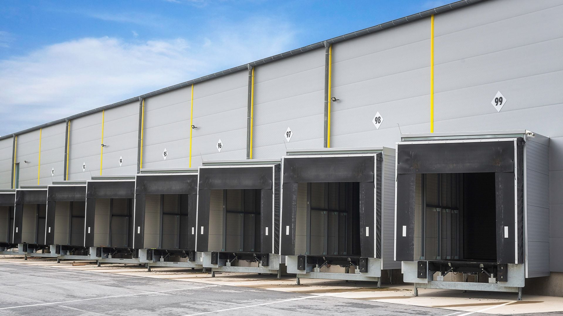An exterior view of a large-scale Europe-based logistics facility, featuring a row of numbered loading docks (92–99) and specialized docking bays, representing high-quality industrial real estate for supply chain operations.