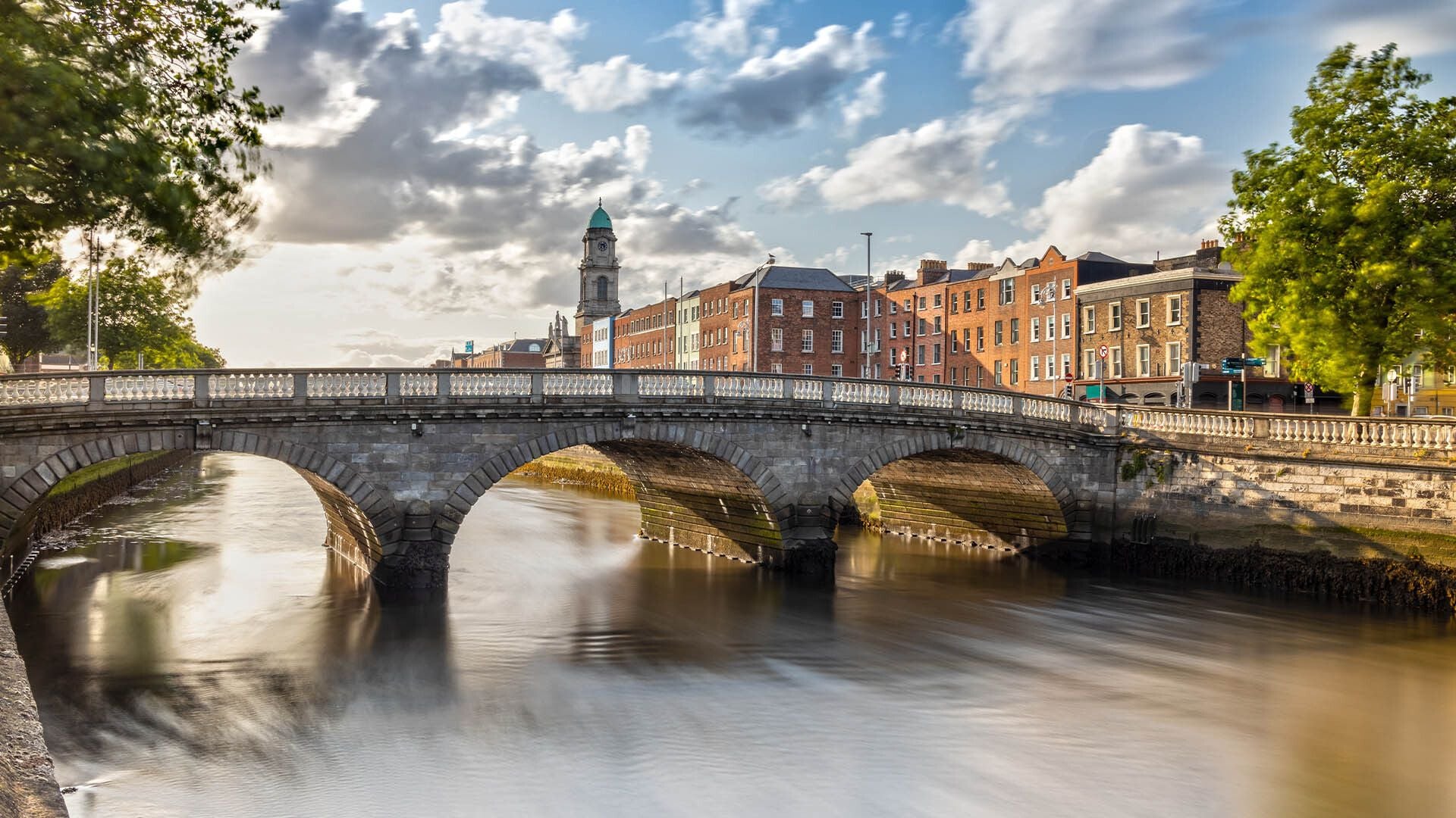 A scenic view of a stone arch bridge crossing the River Liffey in Dublin, with historic city buildings and housing along the quay, representing the urban landscape where tax control and financial regulations are managed.