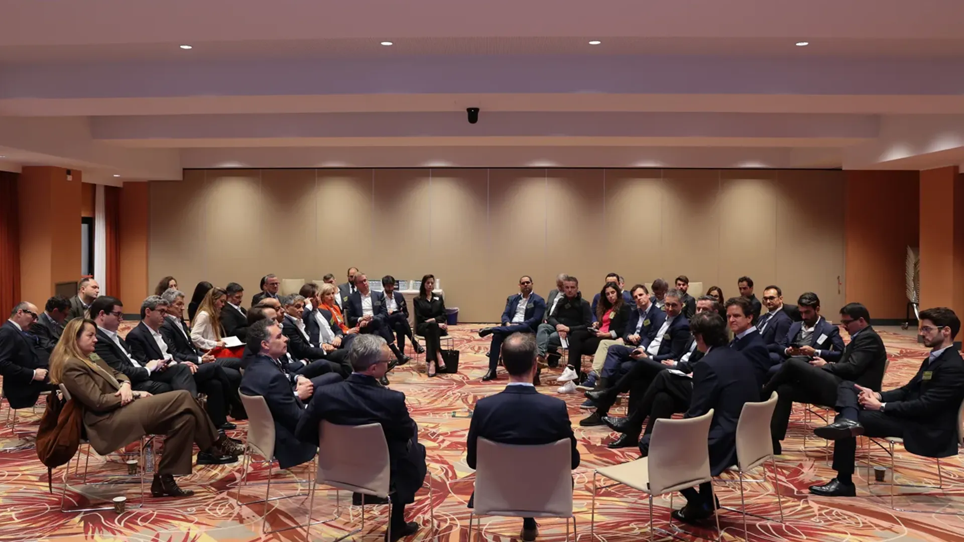 A wide shot of a large group of business leaders seated in a circular arrangement, participating in an intimate forum at the GRI Hospitality Europe 2025 conference to discuss hospitality real estate and investment.