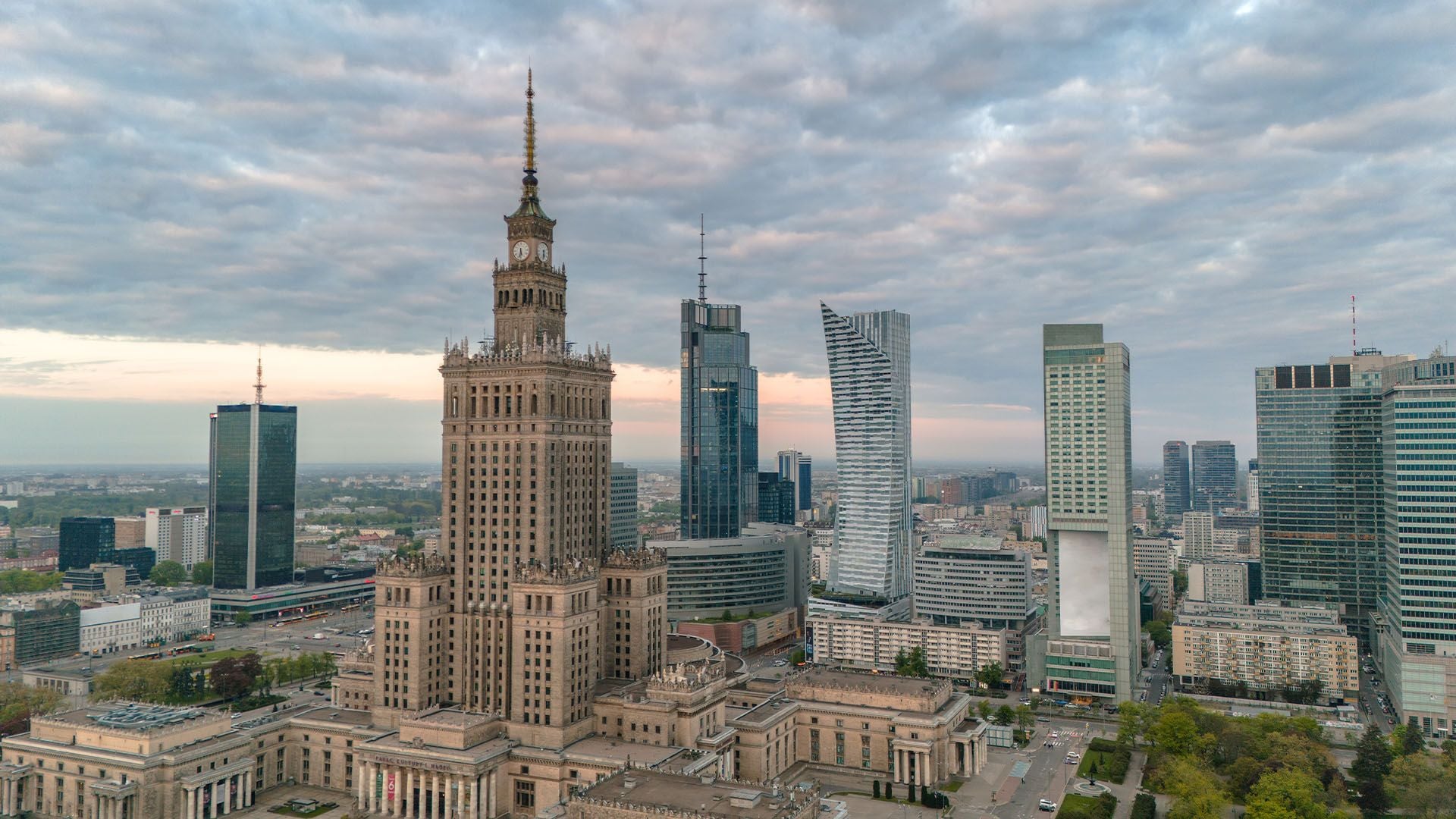 A wide shot of Warsaw’s city centre, contrasting the historic, Soviet-era Palace of Culture and Science with a surrounding cluster of sleek, modern glass skyscrapers. The image represents the rapid architectural evolution of the Polish capital into a primary CEE investment hub.