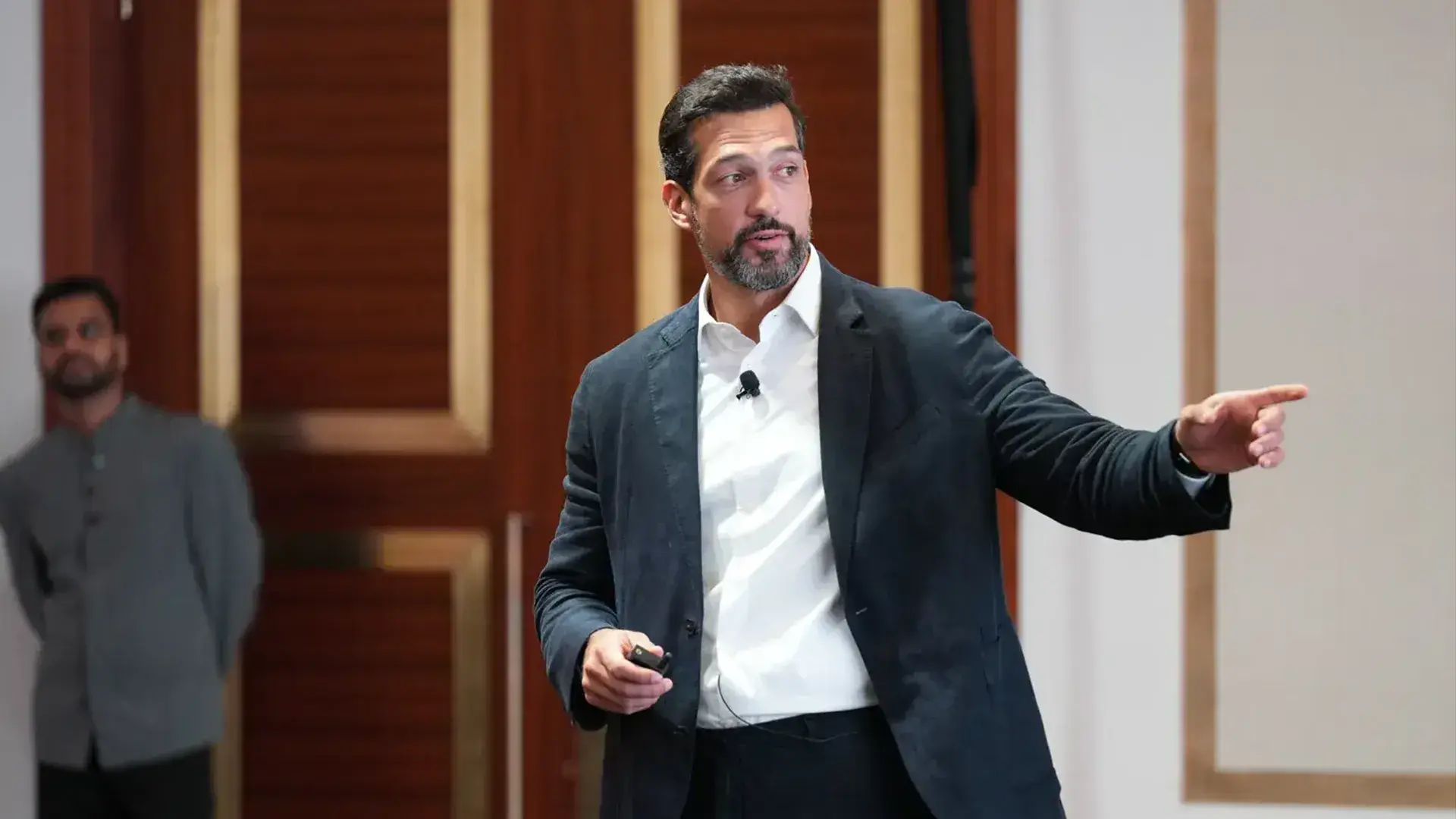 A male speaker presenting and gesturing while holding a remote on stage at a global real estate summit.