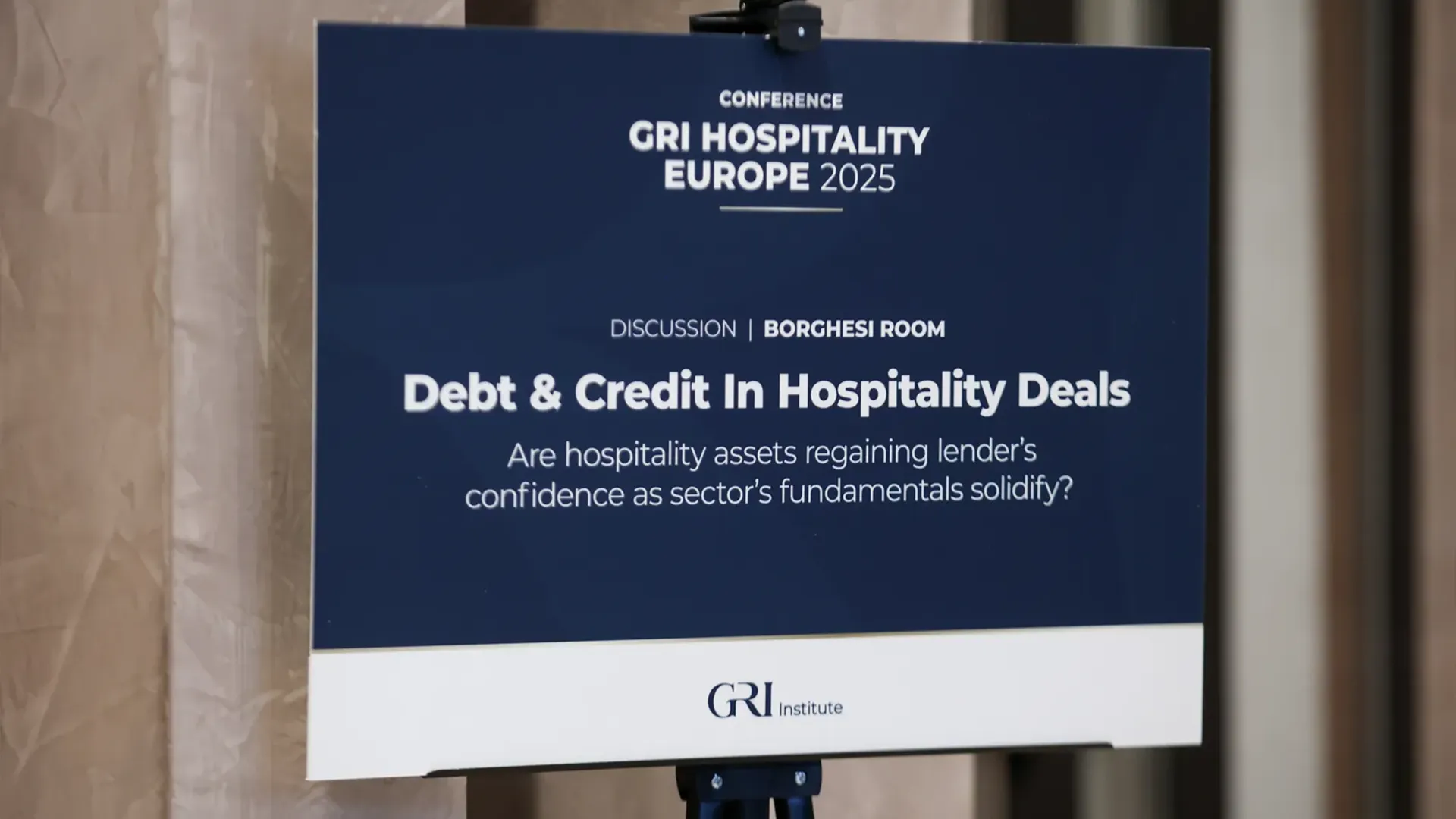 A sign for the "Debt & Credit In Hospitality Deals" discussion in the Borghesi Room at the GRI Hospitality Europe 2025 conference, asking if hospitality real estate assets are regaining lender's confidence.
