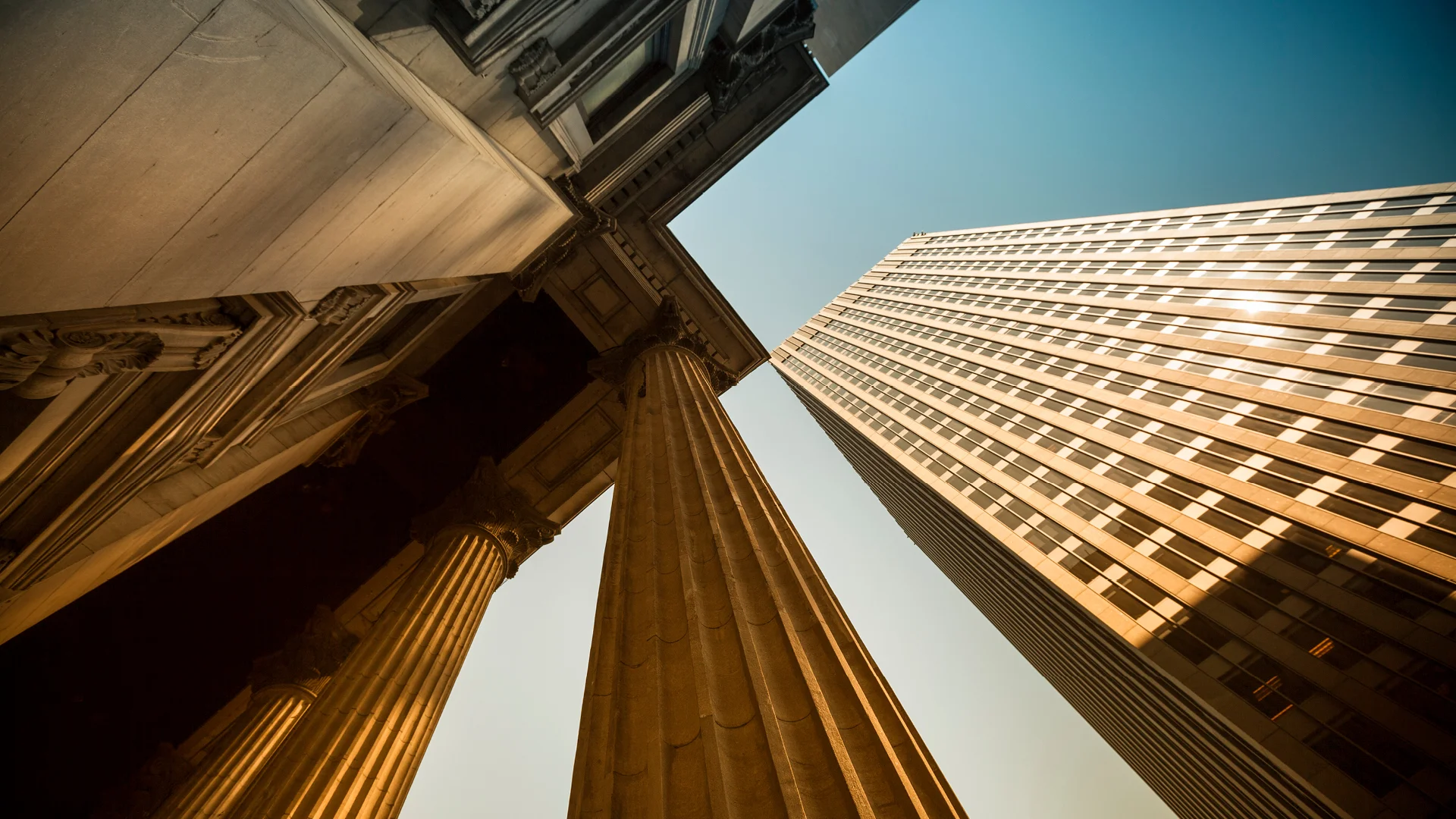 Extreme low-angle shot contrasting classical architectural columns with a modern skyscraper, illustrating the evolution and diversity of urban real estate.