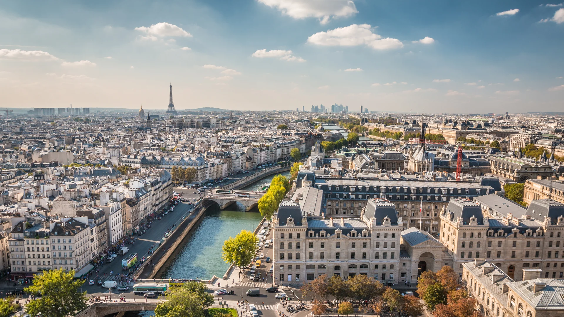High-angle view of the Paris skyline with the Seine River, classic Haussmann buildings, and the Eiffel Tower in the distance, representing prime European real estate investment.
