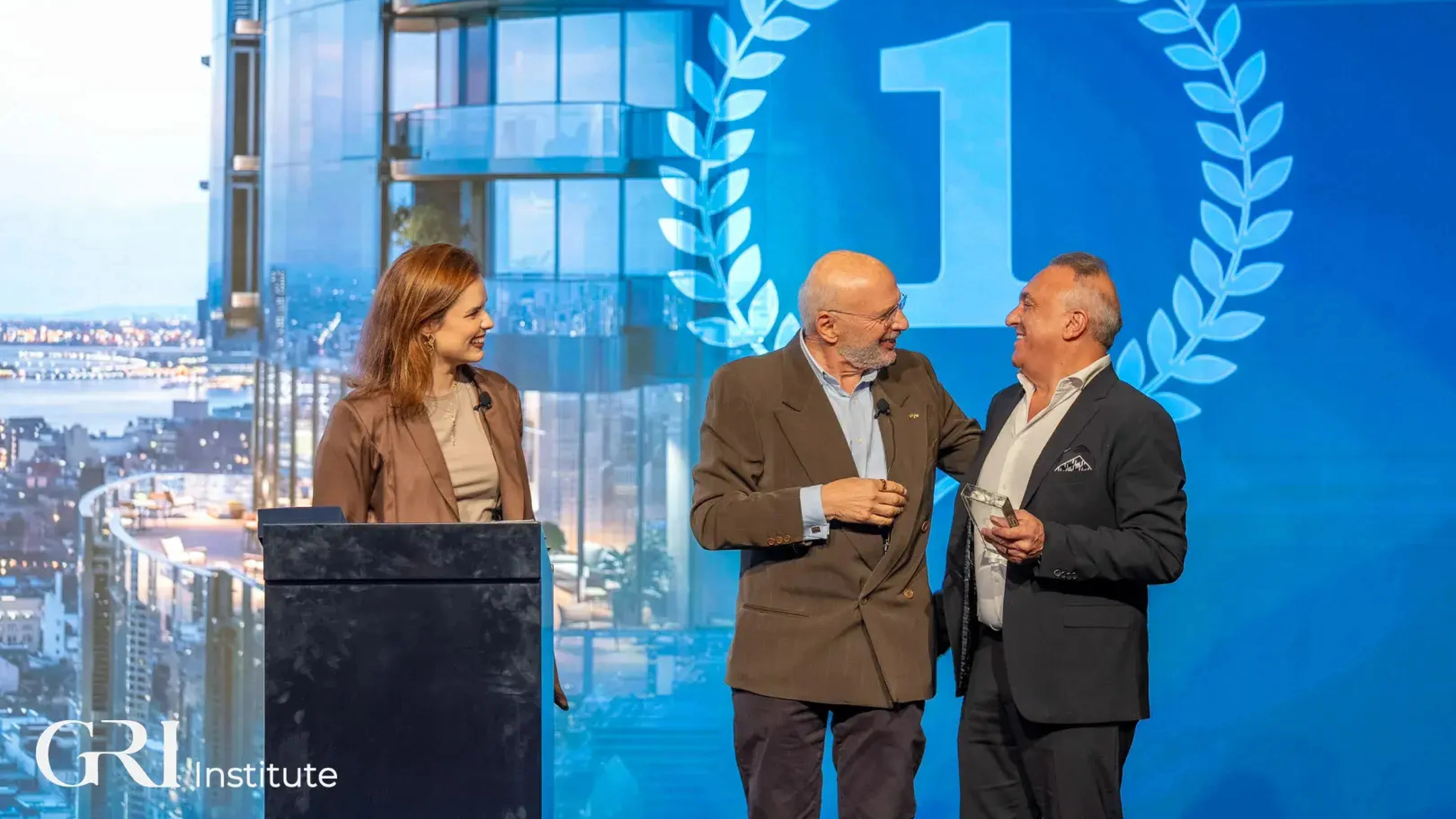  Three people on a stage at a real estate awards ceremony hosted by the GRI Institute, celebrating the BTR Project of the Year winner.