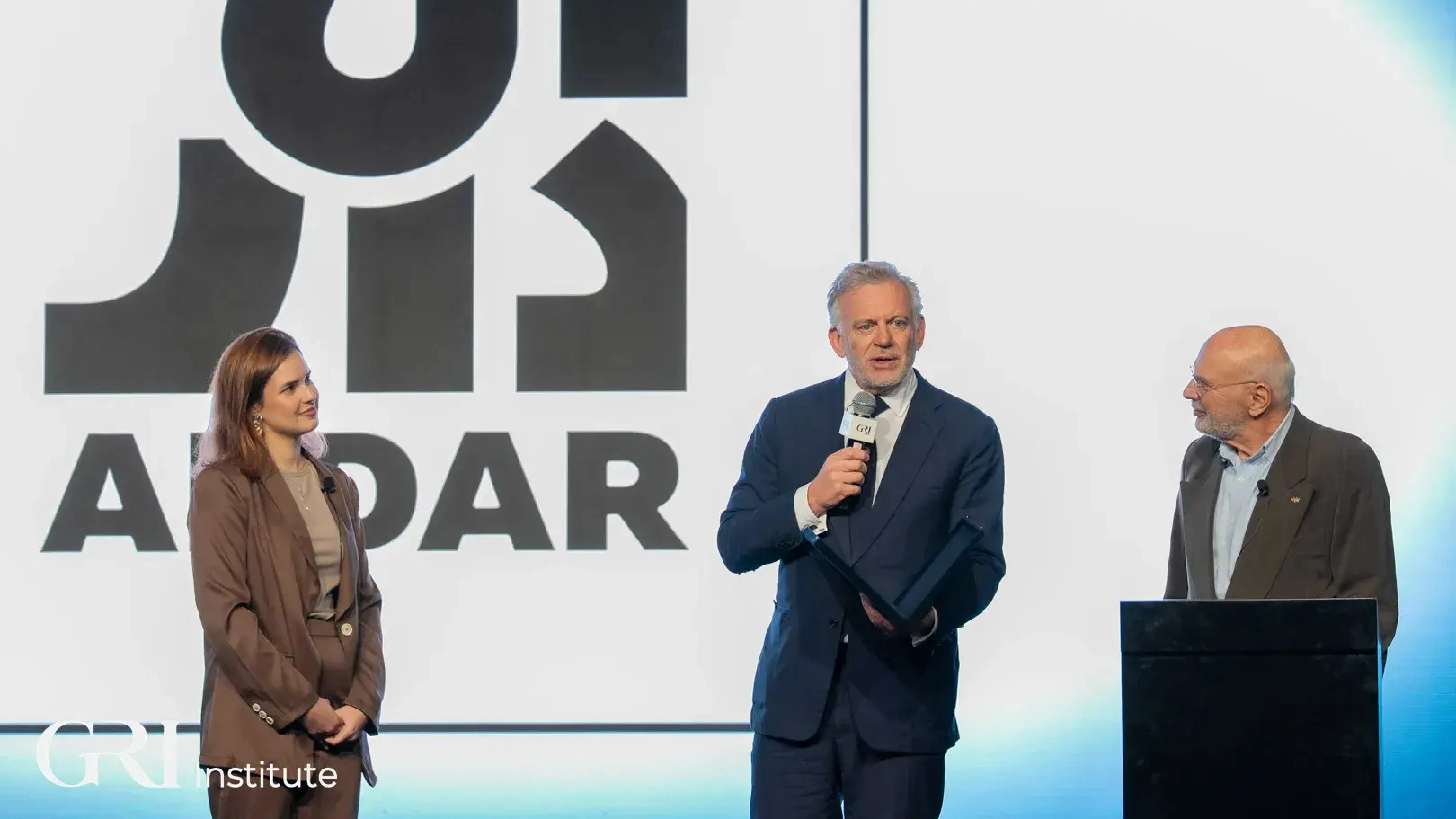 Three people on a stage at a real estate awards ceremony hosted by the GRI Institute, celebrating the Developer of the Year winner.