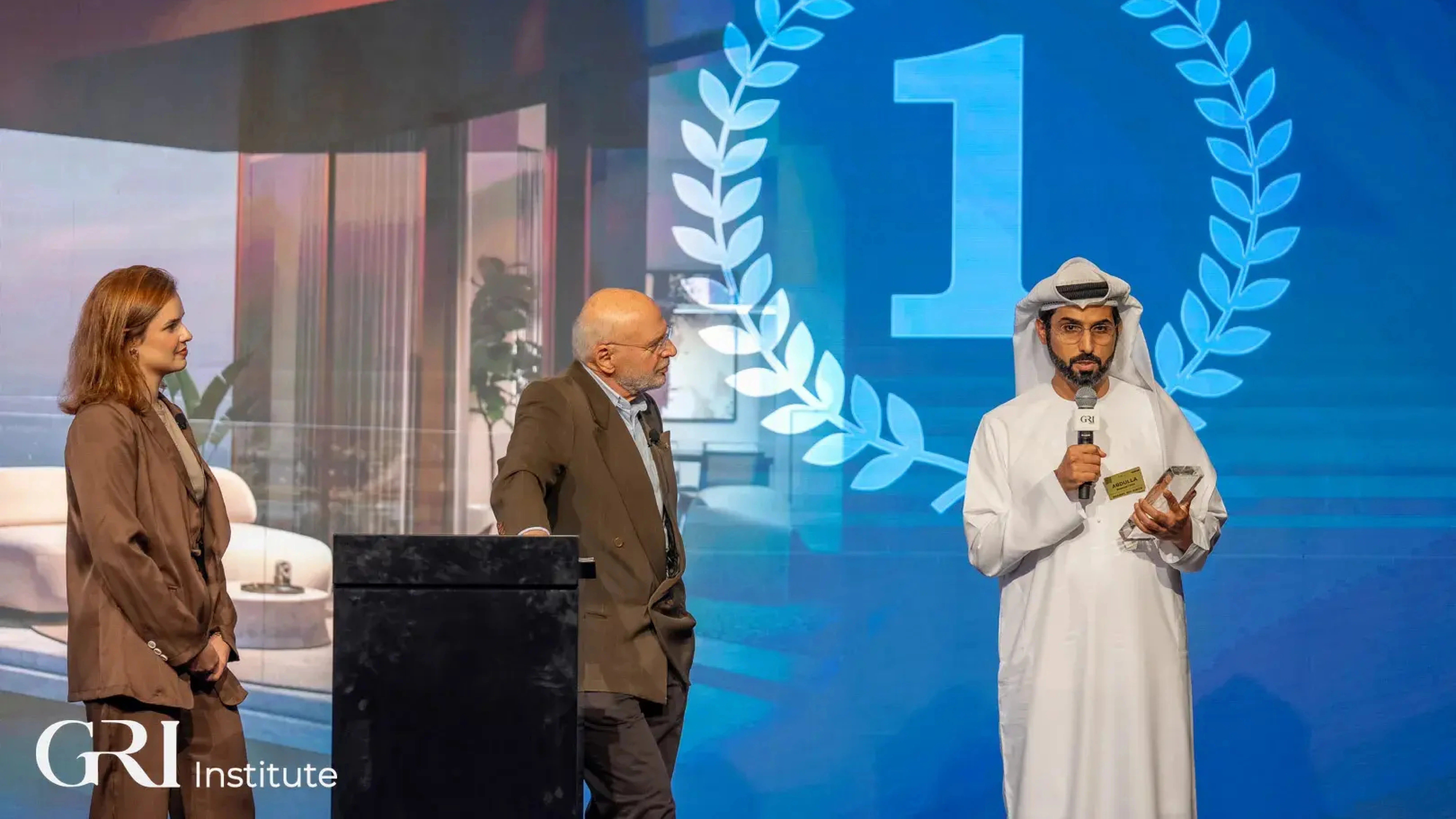 Three people on a stage at a real estate awards ceremony hosted by the GRI Institute, celebrating the Hospitality Project of the Year winner.