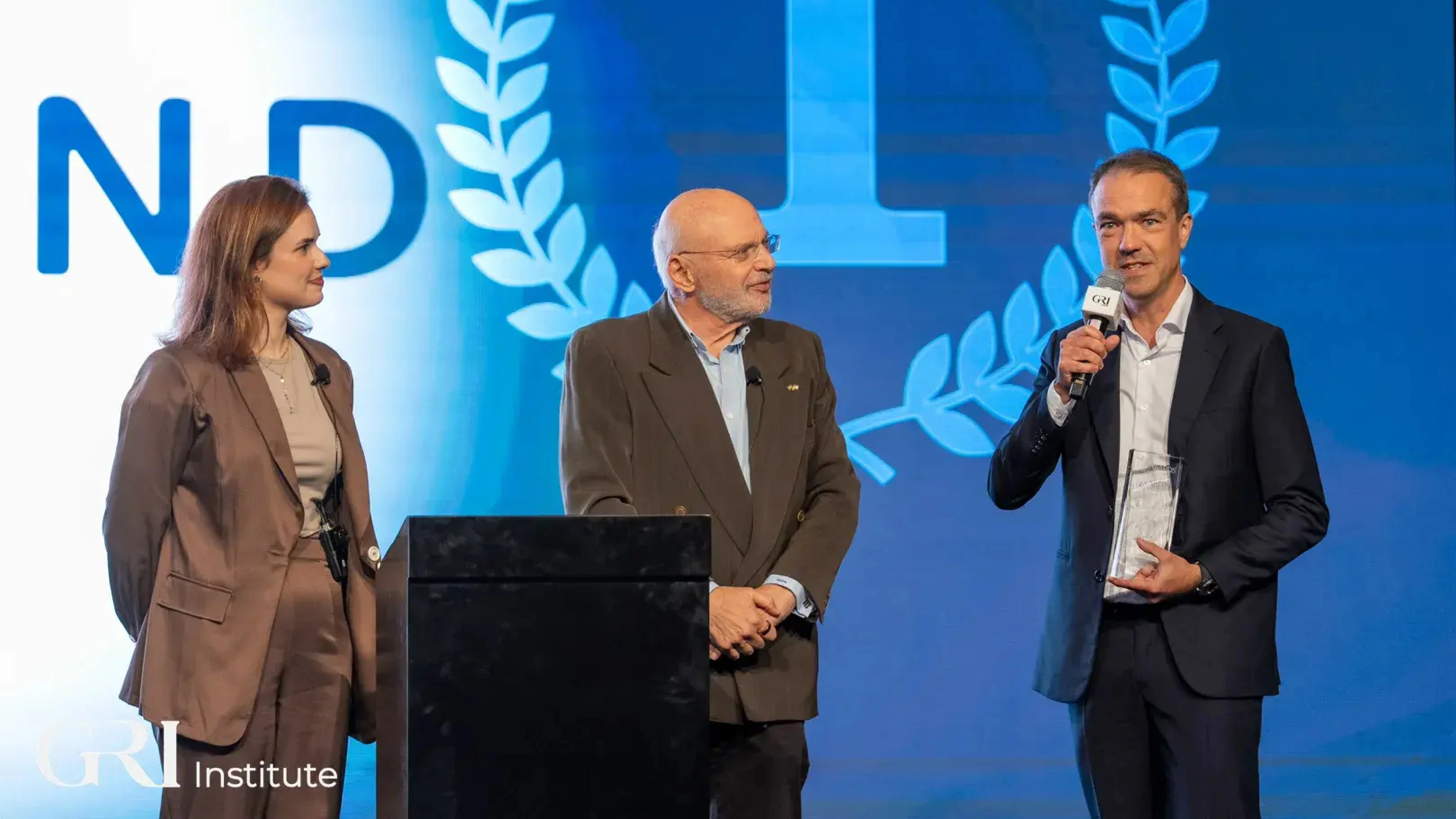 Three people on a stage at a real estate awards ceremony hosted by the GRI Institute, celebrating the PropTech of the Year winner.