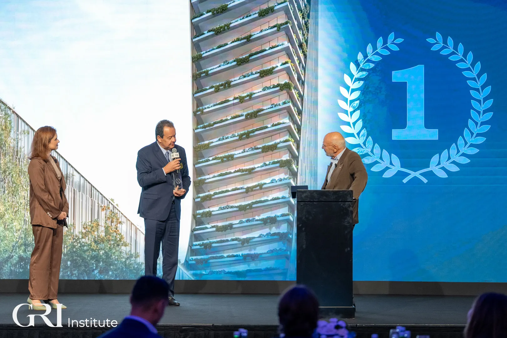 Three people on a stage at a real estate awards ceremony hosted by the GRI Institute, celebrating the Residential Project of the Year winner.