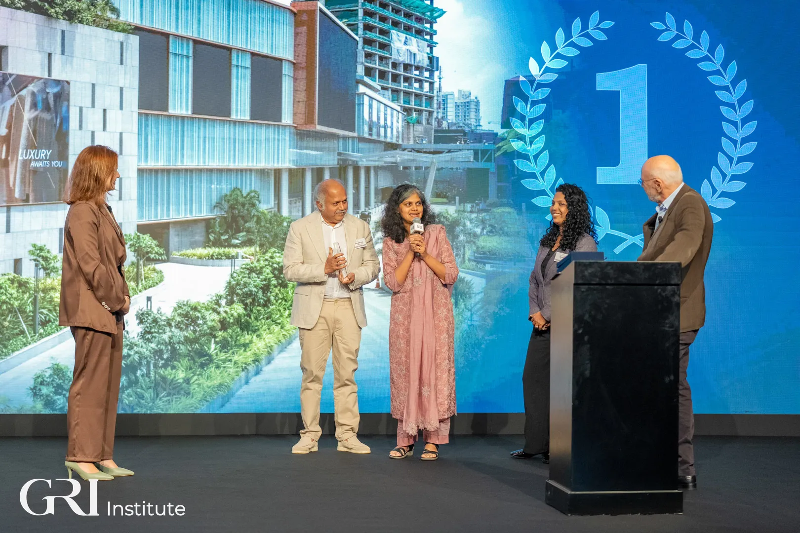 Five people on a stage at a real estate awards ceremony hosted by the GRI Institute, celebrating the Retail Project of the Year winner.