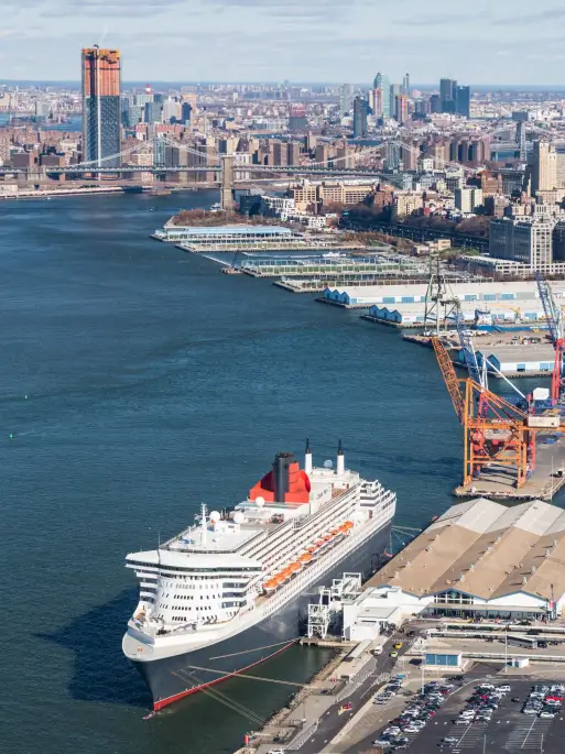 Aerial view of Brooklyn Marine Terminal with shipping containers and warehouses, featuring the Manhattan skyline across the East River.