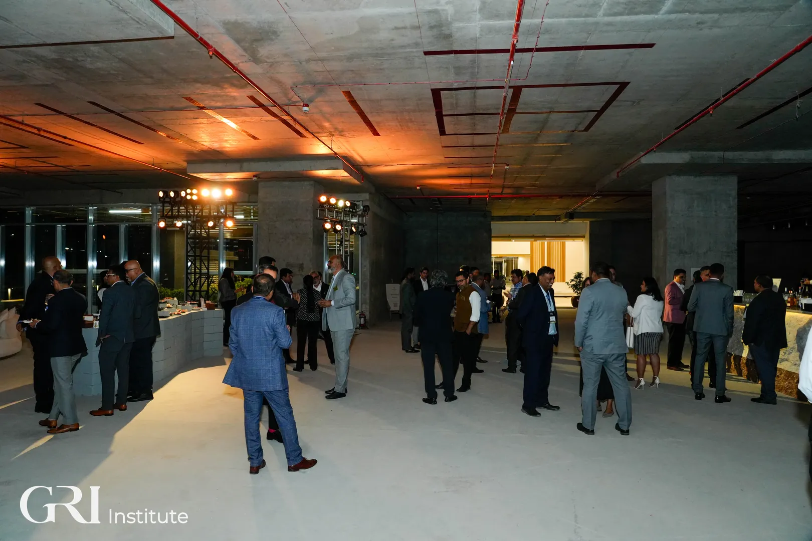 Attendees networking over cocktails at the 77 Town Centre venue, featuring a bespoke lounge and bar area designed within an unfinished concrete space for the Bangalore RE 2026 post-event gathering.