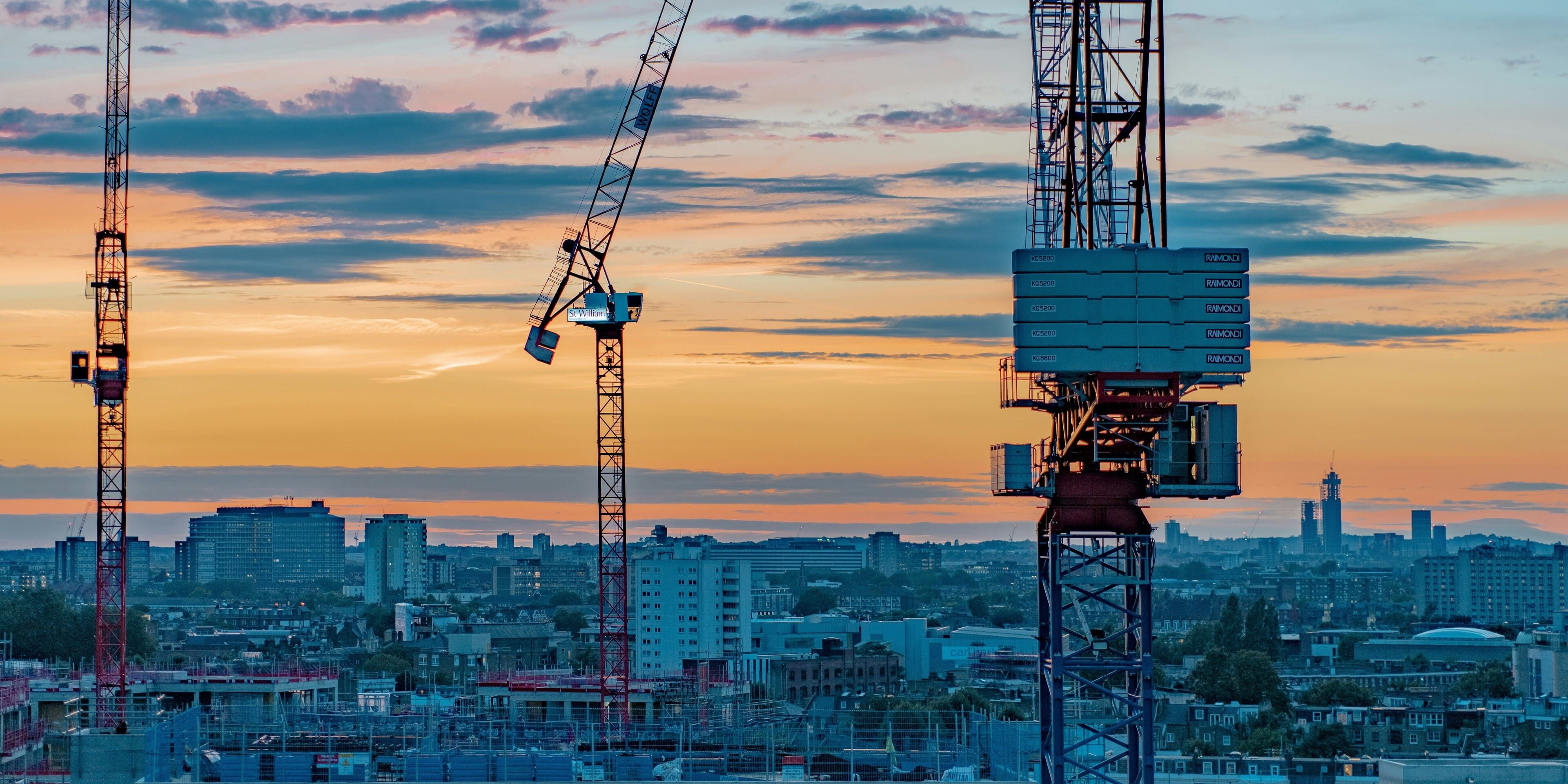 Foto de uma cidade ao fundo com foco em guindastes trabalhando em infraestrutura